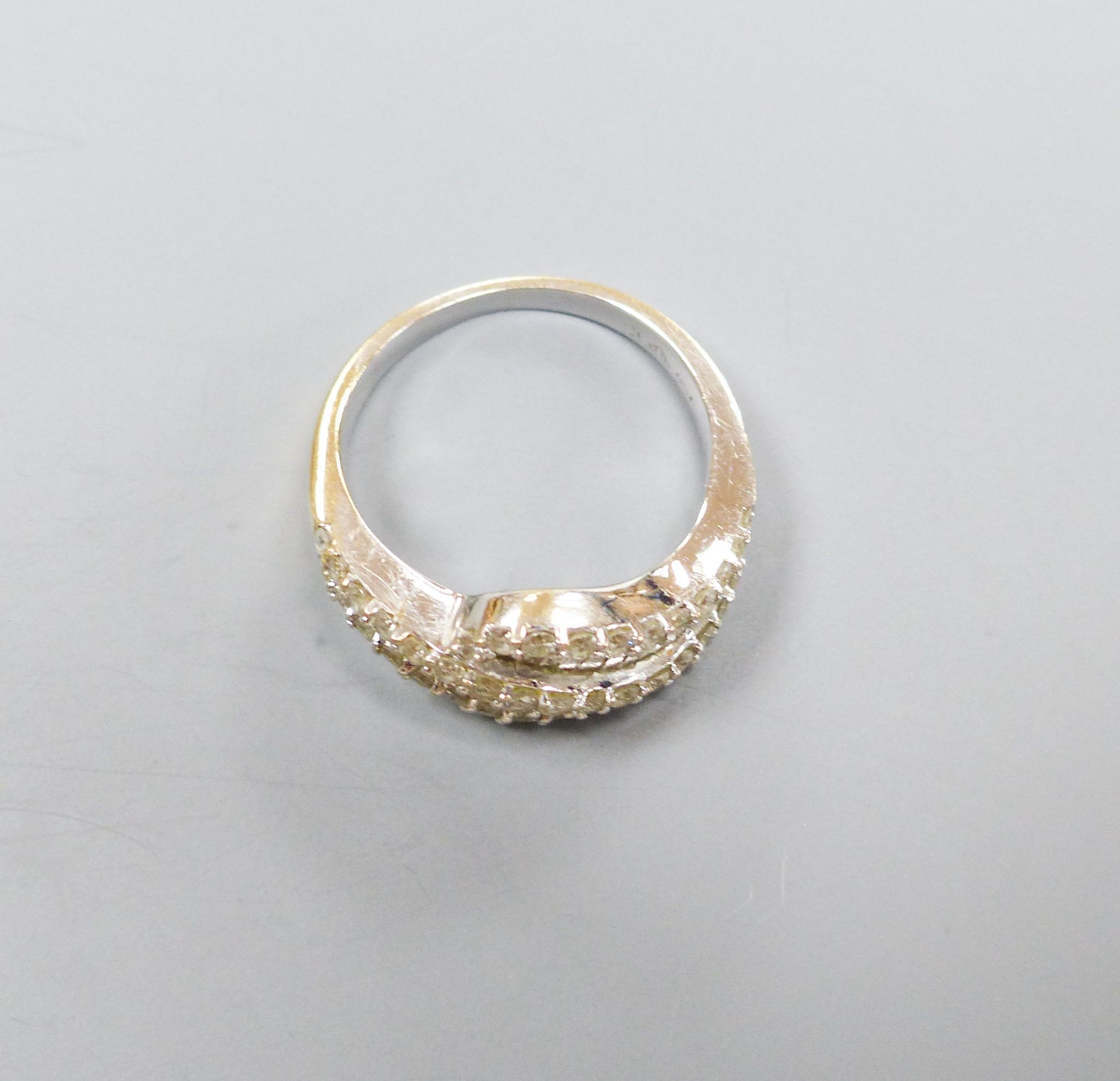 A modern 750 white metal, baguette and round cut diamond set two row crossover ring, size M/N, gross 5.4 grams, (one stone missing).